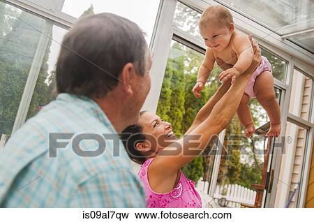 Stock Photo - Mother holding up baby daughter in conservatory. Fotosearch