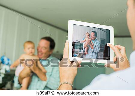 Over shoulder portrait of grandfather and baby granddaughter taken on digital tablet in living room View Large Photo Image Stock Image - Over shoulder portrait of grandfather and baby granddaughter taken on digital tablet in living room. Fotosearch