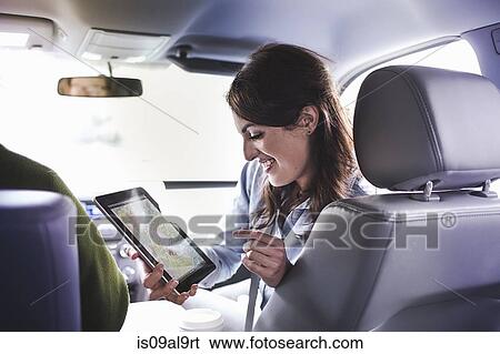 Over shoulder view of young woman in car front seat using digital tablet map View Large Photo Image Stock Photograph - Over shoulder view of young woman in car front seat using digital tablet map. Fotosearch
