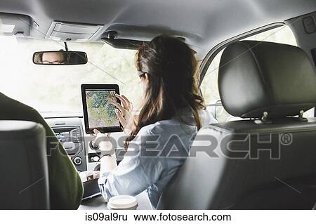 Stock Photograph - Over shoulder view of young woman in car front seat using digital tablet touchscreen map. Fotosearch