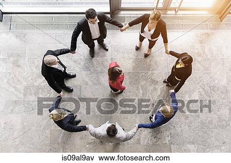Overhead view of business team in circle holding hands surrounding boss View Large Photo Image Stock Photo - Overhead view of business team in circle holding hands surrounding boss. Fotosearch