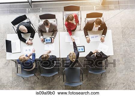 Stock Image - Overhead view of business team shaking hands with client at desk in office. Fotosearch