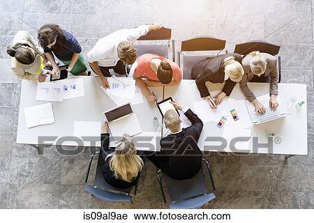 Stock Image - Overhead view of business team brainstorming at desk in office. Fotosearch