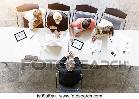 Overhead view of businessmen and women meeting client at desk in office View Large Photo Image Stock Image - Overhead view of businessmen and women meeting client at desk in office. Fotosearch