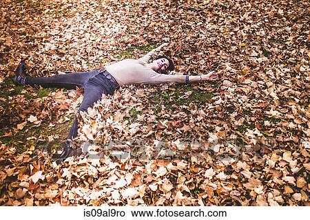 Overhead view of young woman lying on autumn leaves with arms and legs outstretched View Large Photo Image Picture - Overhead view of young woman lying on autumn leaves with arms and legs outstretched. Fotosearch