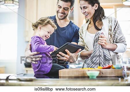 Stock Photography - Parents and daughter using digital tablet in kitchen. Fotosearch
