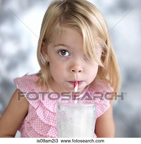 Stock Image - Portrait of female toddler blowing bubbles in milk through drinking straw. Fotosearch