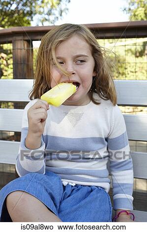 Portrait of girl eating iced lolly on garden bench View Large Photo Image Picture - Portrait of girl eating iced lolly on garden bench. Fotosearch