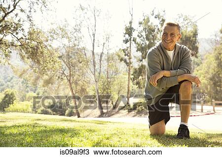 Stock Image - Portrait of mature male runner on one knee in park. Fotosearch