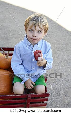 Portrait of smiling boy sitting in pumpkin cart eating iced lolly View Large Photo Image Stock Photography - Portrait of smiling boy sitting in pumpkin cart eating iced lolly. Fotosearch