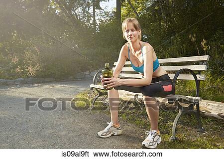 Stock Photograph - Portrait of smiling female runner taking a break on park bench. Fotosearch