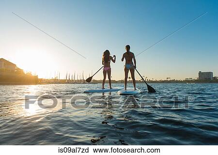 Stock Image - Rear view of two women stand up paddleboarding, Mission Bay, San Diego, California, USA. Fotosearch