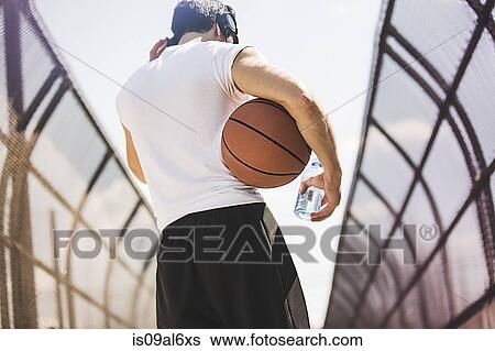 Stock Photograph - Rear view of young male basketball player walking along footbridge listening to headphones. Fotosearch