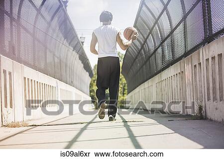 Rear view of young male basketball player walking along footbridge carrying ball View Large Photo Image Stock Photography - Rear view of young male basketball player walking along footbridge carrying ball. Fotosearch