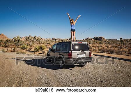 Stock Photograph - Runner jubilant standing on car, Joshua Tree National Park, California, US. Fotosearch