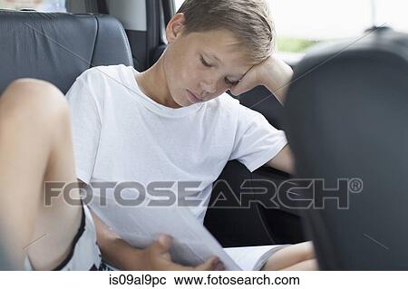 Stock Image - Teenage boy reading in back seat of car. Fotosearch