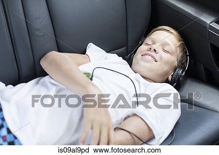 Teenage boy smiling whilst listening to headphones in back seat of car View Large Photo Image Stock Image - Teenage boy smiling whilst listening to headphones in back seat of car. Fotosearch