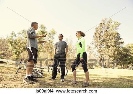 Picture - Three mature cyclists chatting in park. Fotosearch