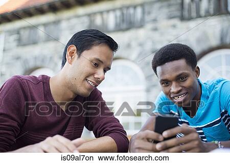 Picture - Two male friends using smartphone. Fotosearch