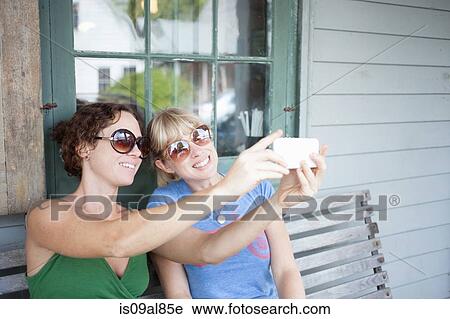 Stock Image - Two mid adult woman taking smartphone selfie on porch. Fotosearch