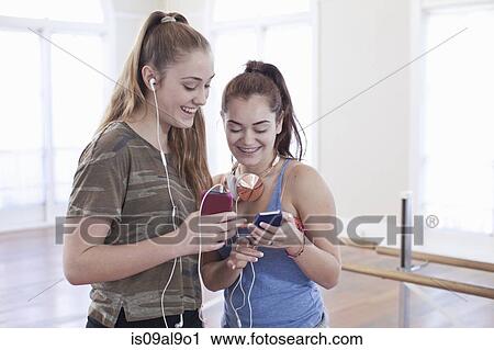 Stock Image - Two teenage girls listening to earphones in ballet school. Fotosearch