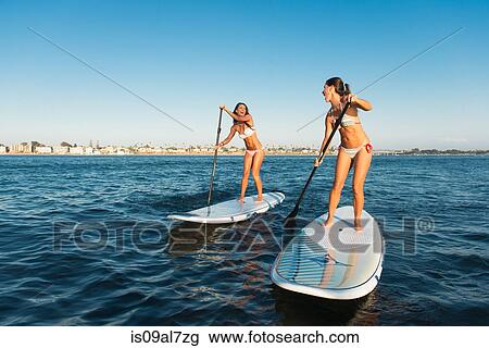 Stock Image - Two women chatting whilst stand up paddleboarding, Mission Bay, San Diego, California, USA. Fotosearch