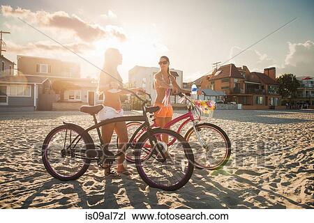 Stock Image - Two women cyclists chatting on beach, Mission Bay, San Diego, California, USA. Fotosearch