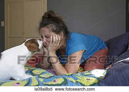 Stock Photography - Woman pulling face whilst being licked by dog. Fotosearch
