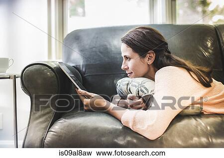 Woman using digital tablet on sofa View Large Photo Image Stock Photo - Woman using digital tablet on sofa. Fotosearch