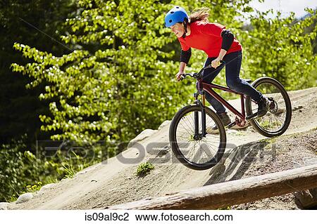 Stock Image - Young female bmx biker speeding down rocks in forest. Fotosearch