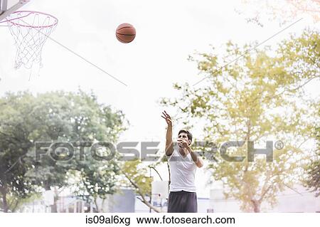 Stock Image - Young male basketball player throwing ball towards basketball net. Fotosearch