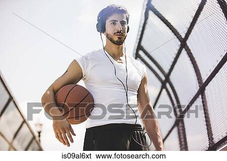 Stock Photograph - Young male basketball player walking along footbridge listening to headphones. Fotosearch