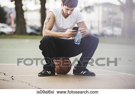 Young male basketball sitting on ball texting on smartphone View Large Photo Image Stock Image - Young male basketball sitting on ball texting on smartphone. Fotosearch