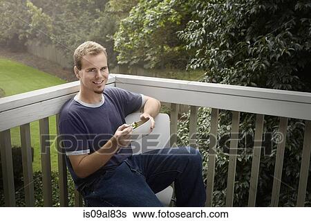 Stock Photograph - Young man having salad on balcony. Fotosearch