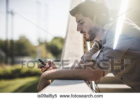Young man leaning on footbridge wall selecting music on smartphone View Large Photo Image Stock Photography - Young man leaning on footbridge wall selecting music on smartphone. Fotosearch