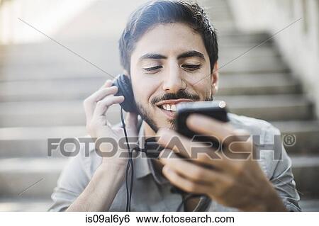 Young man sitting on footbridge stairs listening to music on headphones View Large Photo Image Stock Photograph - Young man sitting on footbridge stairs listening to music on headphones. Fotosearch