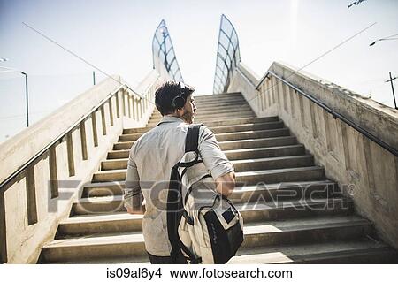 Young man walking up footbridge stairs listening to music on headphones View Large Photo Image Picture - Young man walking up footbridge stairs listening to music on headphones. Fotosearch