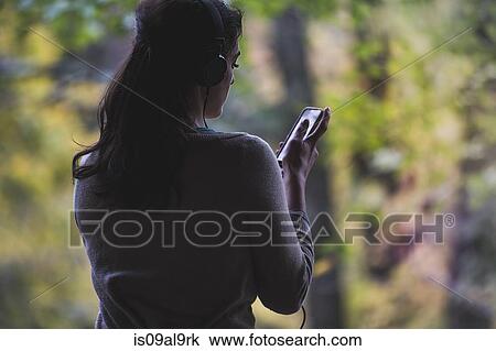 Young woman in forest looking at smartphone whilst listening to headphones View Large Photo Image Stock Image - Young woman in forest looking at smartphone whilst listening to headphones. Fotosearch