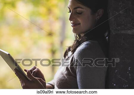 Young woman leaning against wall using touchscreen on digital tablet View Large Photo Image Stock Image - Young woman leaning against wall using touchscreen on digital tablet. Fotosearch