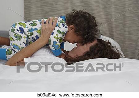 Stock Image - Young woman lying on bed face to face with toddler son. Fotosearch