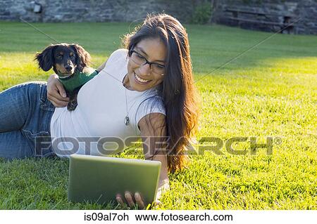 Young woman lying on grass using digital tablet with pet dog View Large Photo Image Stock Image - Young woman lying on grass using digital tablet with pet dog. Fotosearch