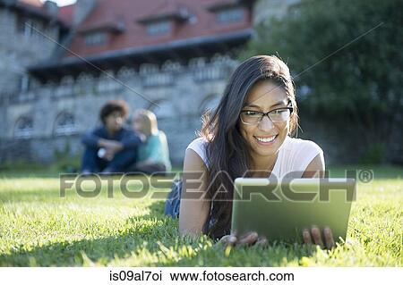 Stock Image - Young woman lying on grass using digital tablet. Fotosearch
