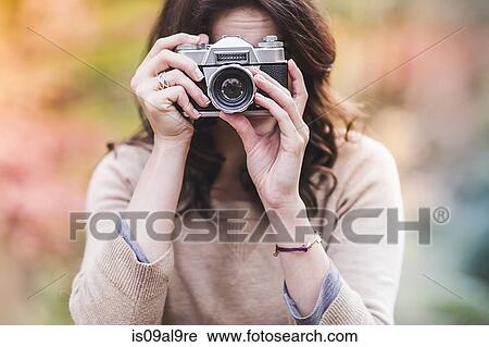 Stock Image - Young woman photographing with SLR camera in autumn forest. Fotosearch