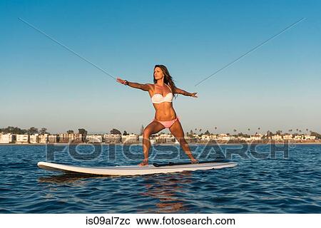 Stock Image - Young woman practicing yoga position on paddleboard, Mission Bay, San Diego, California, USA. Fotosearch