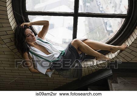 Stock Photography - Young woman reclining by round window. Fotosearch