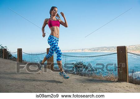 Young woman running on path by sea View Large Photo Image Stock Photo - Young woman running on path by sea. Fotosearch