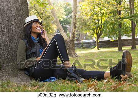 Young woman sitting against tree using smartphone View Large Photo Image Stock Image - Young woman sitting against tree using smartphone. Fotosearch