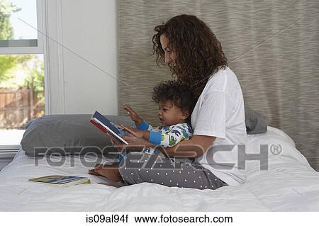 Young woman sitting on bed reading book to toddler son View Large Photo Image Stock Image - Young woman sitting on bed reading book to toddler son. Fotosearch