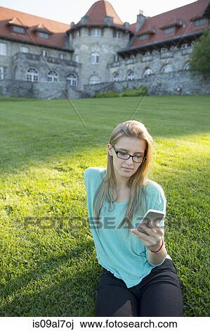 Young woman sitting on grass using smartphone View Large Photo Image Stock Image - Young woman sitting on grass using smartphone. Fotosearch