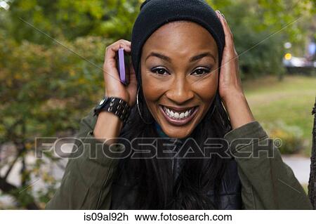 Stock Image - Young woman smiling and holding smartphone to ear. Fotosearch